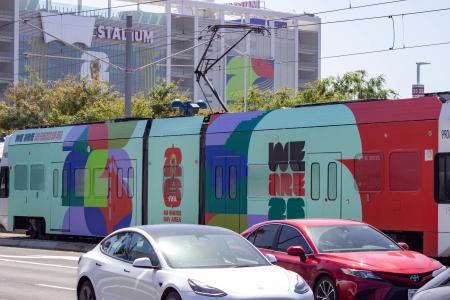 wrapped train with FIFA design, cars in foreground, stadium in background