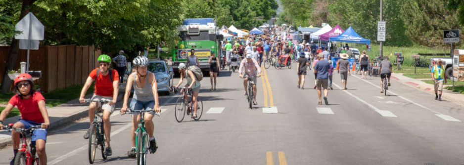 S2C9.7G2_revisingLOS_CaseStudy2_FC Photo of a roadway with hundreds of people walking or riding bicycles while wearing helmets with a food truck and tents in the background