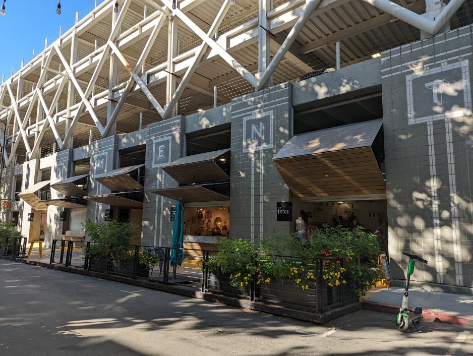 Photo of a grey and white parking structure with retail shops integrated in the bottom floor with wooden awnings over the open windows
