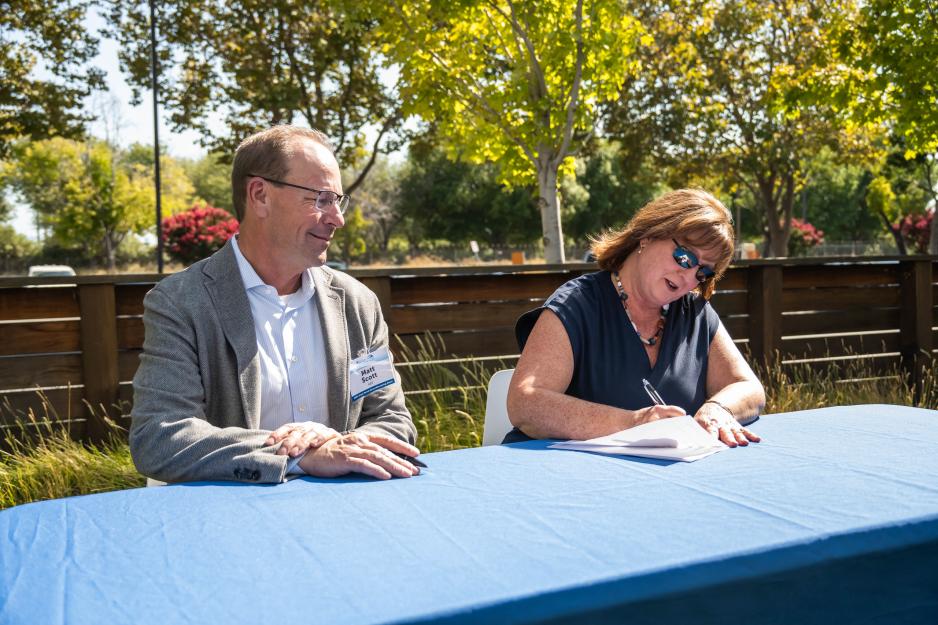 Woman and man sitting at a table; woman signing a paper